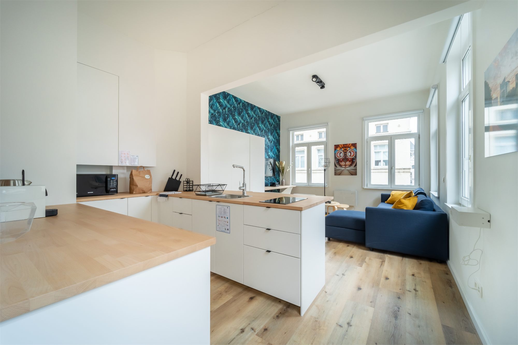 Cuisine ouverte au plan de travail en bois clair, donnant sur un salon avec canapé bleu