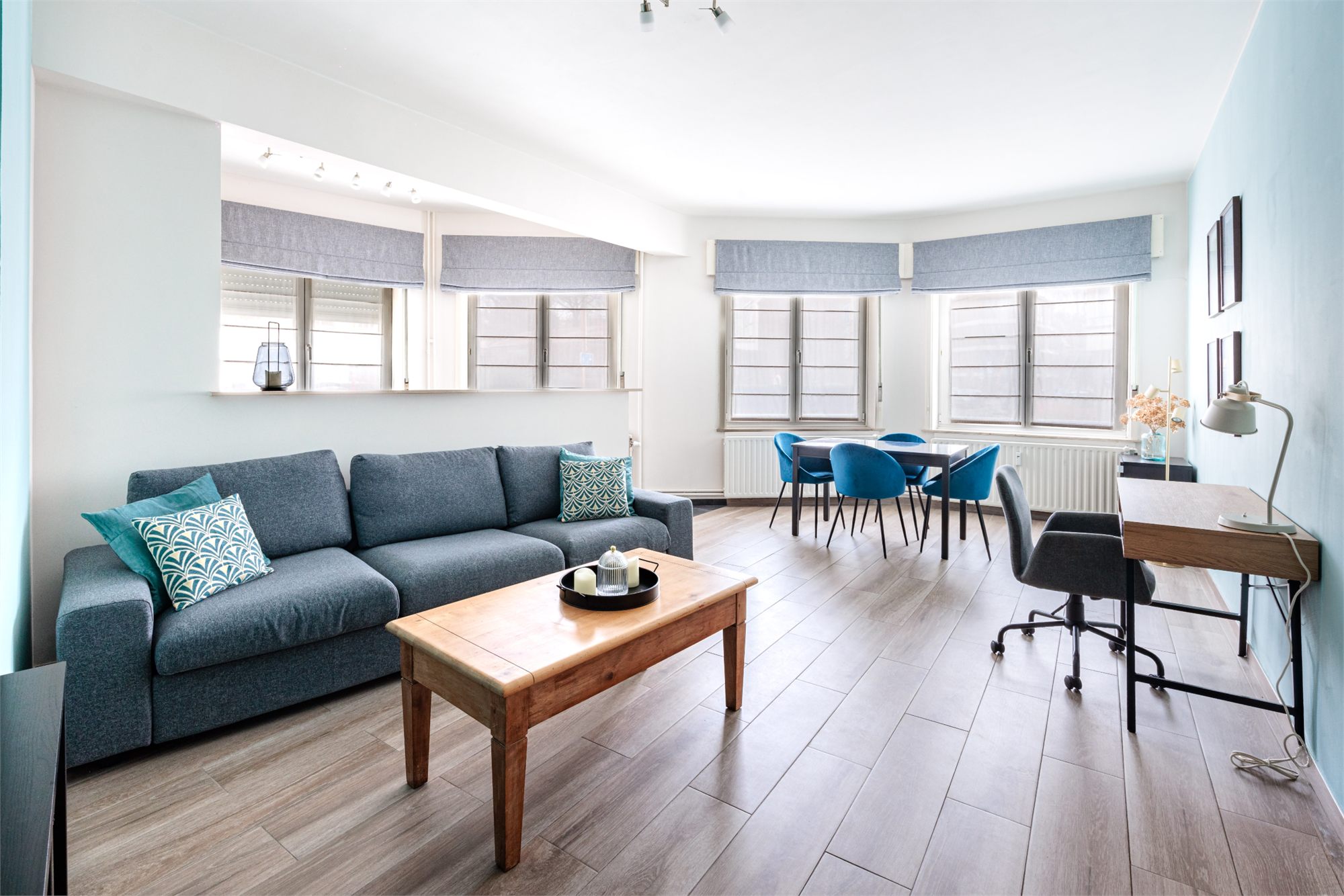 Salon spacieux avec canapé gris-bleu, table basse en bois et coin repas aux chaises bleues
