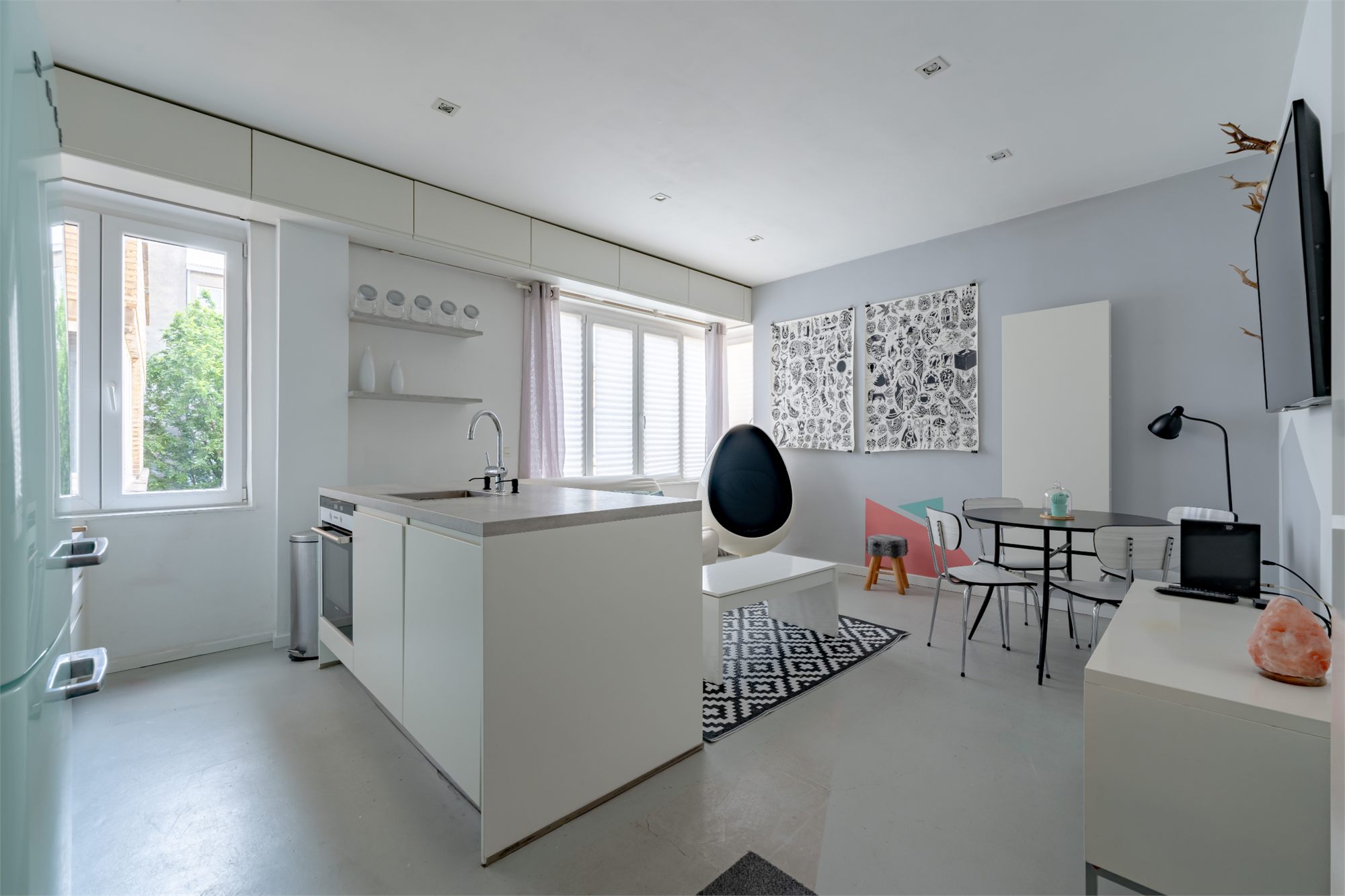 Séjour lumineux avec cuisine ouverte blanche, fauteuil œuf et coin repas